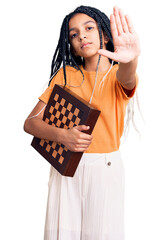 Cute african american girl holding chess with open hand doing stop sign with serious and confident...