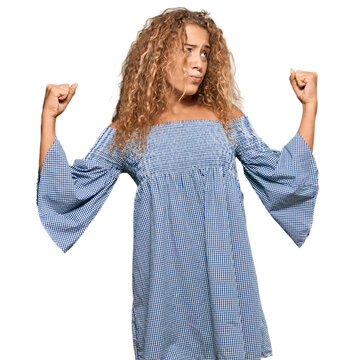 Beautiful caucasian teenager girl wearing summer dress showing arms muscles smiling proud. fitness concept.