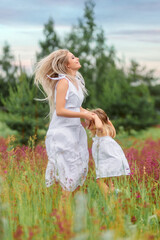 Fototapeta na wymiar Mom and daughter jumping in white clothes in a beautiful flower field in summer or spring