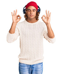 Young hispanic man listening to music using headphones relax and smiling with eyes closed doing meditation gesture with fingers. yoga concept.