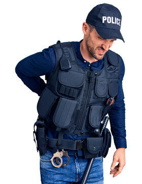 Young handsome man wearing police uniform suffering of backache, touching back with hand, muscular pain