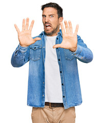 Young handsome man wearing casual denim jacket afraid and terrified with fear expression stop...