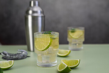 two fresh cold glasses of mahito with lime and ice and shaker on a gray-green background.