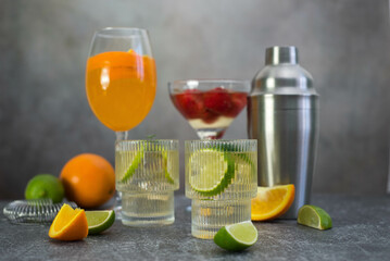 assorted cocktails: two glasses of mojito, orange cocktail, cocktail with strawberries, fruits and shaker on a gray background.