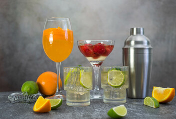 assorted cocktails: two glasses of mojito, orange cocktail, cocktail with strawberries, fruits and shaker on a gray background.