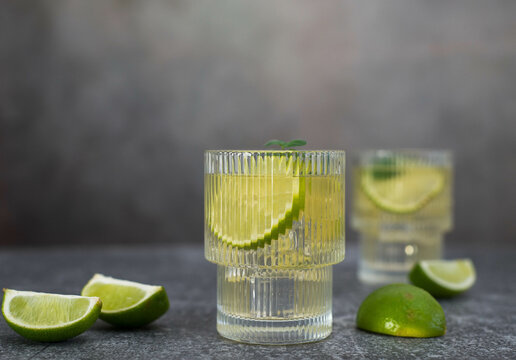 two fresh cold glasses of mahito with lime and ice on a gray-green background.