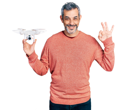 Middle age hispanic man with grey hair holding drone doing ok sign with fingers, smiling friendly gesturing excellent symbol