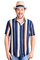 Young handsome caucasian man wearing summer hat sticking tongue out happy with funny expression. emotion concept.
