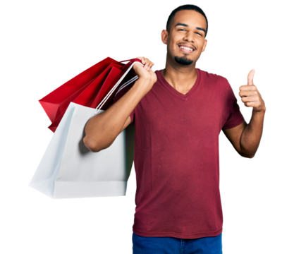 Young african american man holding shopping bags smiling happy and positive, thumb up doing excellent and approval sign