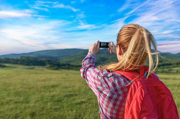 A traveler girl photographs a natural landscape on her phone.