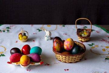 Colored easter eggs in a wooden basket at a white tablecloth on a black background
