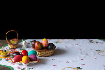 Colored easter eggs in a wooden basket at a white tablecloth on a black background