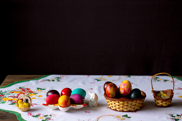 Colored easter eggs in a wooden basket at a white tablecloth on a black background