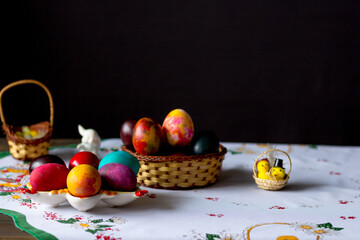 Colored easter eggs in a wooden basket at a white tablecloth on a black background