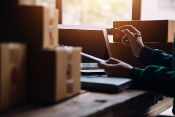 Startup SME small business entrepreneur of freelance Asian woman wearing apron using laptop and box to receive and review orders online to prepare to pack sell to customers, online sme business ideas.