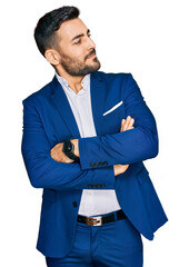 Young hispanic man wearing business jacket looking to the side with arms crossed convinced and...