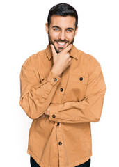 Young hispanic man wearing casual clothes looking confident at the camera smiling with crossed arms and hand raised on chin. thinking positive.