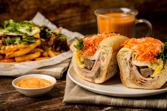 Vietnamese food - Ham headcheese BBQ pork sandwich, Kimchi fries with beef and egg and thai iced tea on the wooden table
