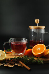 Fruit tea is poured into a transparent glass next to fruits on a black background.