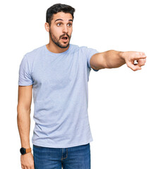 Young hispanic man wearing casual clothes pointing with finger surprised ahead, open mouth amazed expression, something on the front