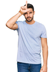 Obraz premium Young hispanic man wearing casual clothes making fun of people with fingers on forehead doing loser gesture mocking and insulting.