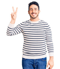 Naklejka premium Young hispanic man wearing casual clothes smiling looking to the camera showing fingers doing victory sign. number two.