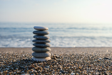 Balanced pebble pyramid silhouette on the beach with the ocean in the background. Zen stones on the sea beach, meditation, spa, harmony, calmness, balance concept.	