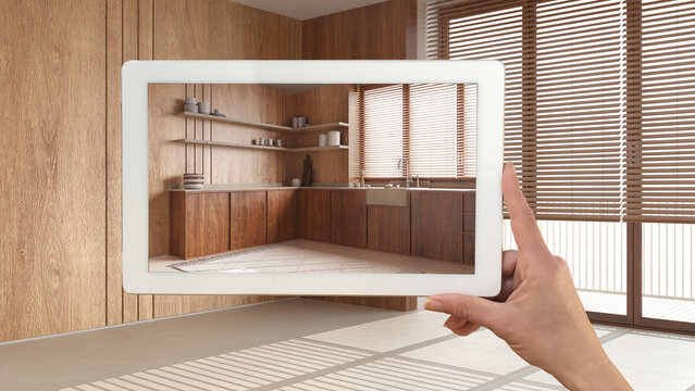 Augmented reality concept. Hand holding tablet with AR application used to simulate furniture and design products in empty wooden interior with marble floor, farmhouse kitchen