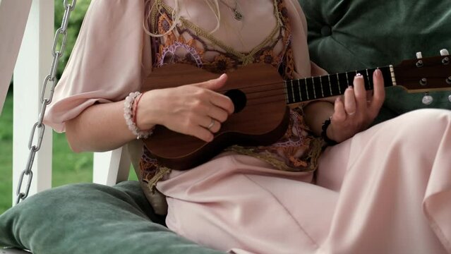 A woman in an elegant boho style dress plays the ukulele.
