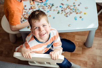 a boy of 6 years old collects a puzzle at home and looks at the camera with a smile