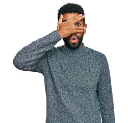 Young african american man wearing casual clothes peeking in shock covering face and eyes with hand, looking through fingers with embarrassed expression.