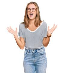 Beautiful young blonde woman wearing casual clothes and glasses crazy and mad shouting and yelling with aggressive expression and arms raised. frustration concept.