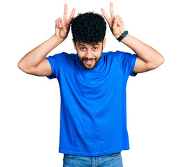 Young arab man with beard wearing casual blue t shirt posing funny and crazy with fingers on head as bunny ears, smiling cheerful