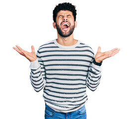 Naklejka premium Young arab man with beard wearing casual striped sweater celebrating mad and crazy for success with arms raised and closed eyes screaming excited. winner concept