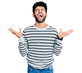 Young arab man with beard wearing casual striped sweater celebrating mad and crazy for success with arms raised and closed eyes screaming excited. winner concept