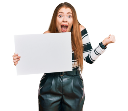 Young beautiful redhead woman holding blank empty banner screaming proud, celebrating victory and success very excited with raised arms