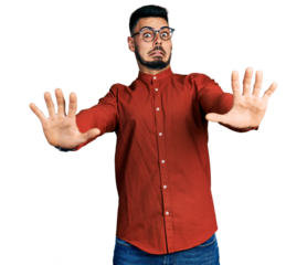 Young hispanic man with beard wearing business shirt and glasses afraid and terrified with fear expression stop gesture with hands, shouting in shock. panic concept.