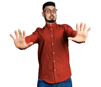 Young hispanic man with beard wearing business shirt and glasses afraid and terrified with fear expression stop gesture with hands, shouting in shock. panic concept.