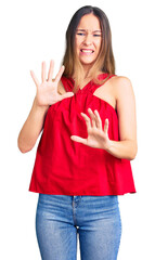 Beautiful brunette young woman wearing casual clothes disgusted expression, displeased and fearful doing disgust face because aversion reaction. with hands raised