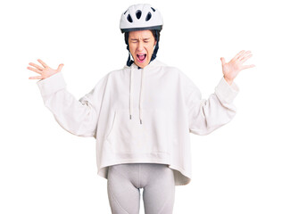 Beautiful brunette young woman wearing bike helmet and sporty clothes celebrating mad and crazy for success with arms raised and closed eyes screaming excited. winner concept