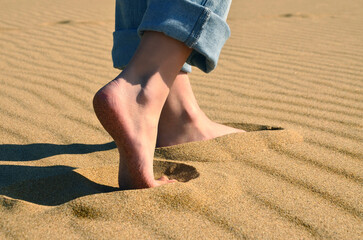 Fototapeta na wymiar Barefoot girl in jeans walking in the sands on the coast