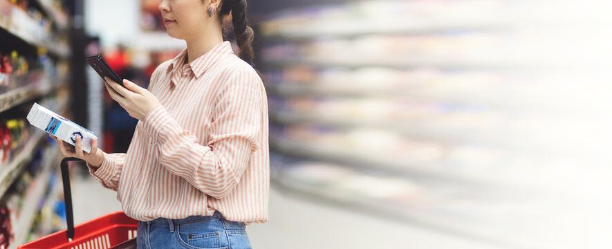 Web banner of modern shopping. Side view of caucasian woman scans qr code of product using smartphone. Shelves with food in background. Copy space and mock up