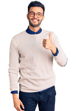 Young handsome hispanic man wearing elegant clothes and glasses doing happy thumbs up gesture with hand. approving expression looking at the camera showing success.