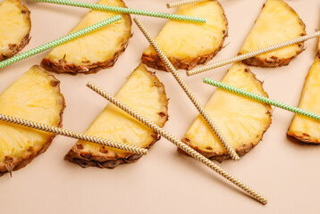 Pieces of pineapple on a beige background and cocktail straws