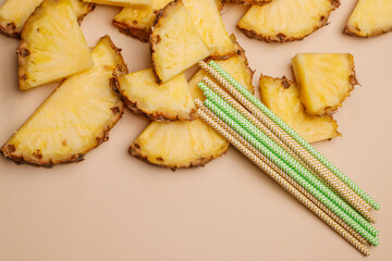 Pieces of pineapple on a beige background and cocktail straws