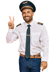 Handsome man with beard wearing airplane pilot uniform showing and pointing up with fingers number...