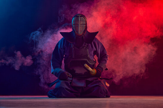 Man, professional kendo athlete, combat sportsman posing with shinai sword against gradient dark background in neon light with smoke. Concept of martial arts, sport, Japanese culture, action and