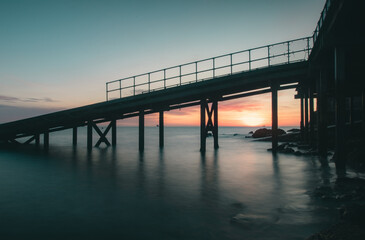 View of a pier leading out at sea at sunrise.