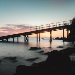 Fototapeta premium View of a pier leading out at sea at sunrise.