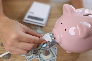 Woman holding power plug and putting on charge pink piggy bank